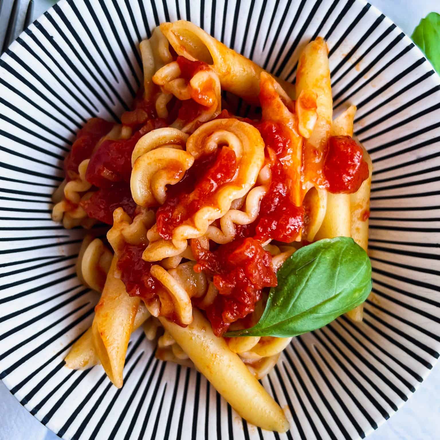 Penne Pomodoro in white and black striped bowl with basil